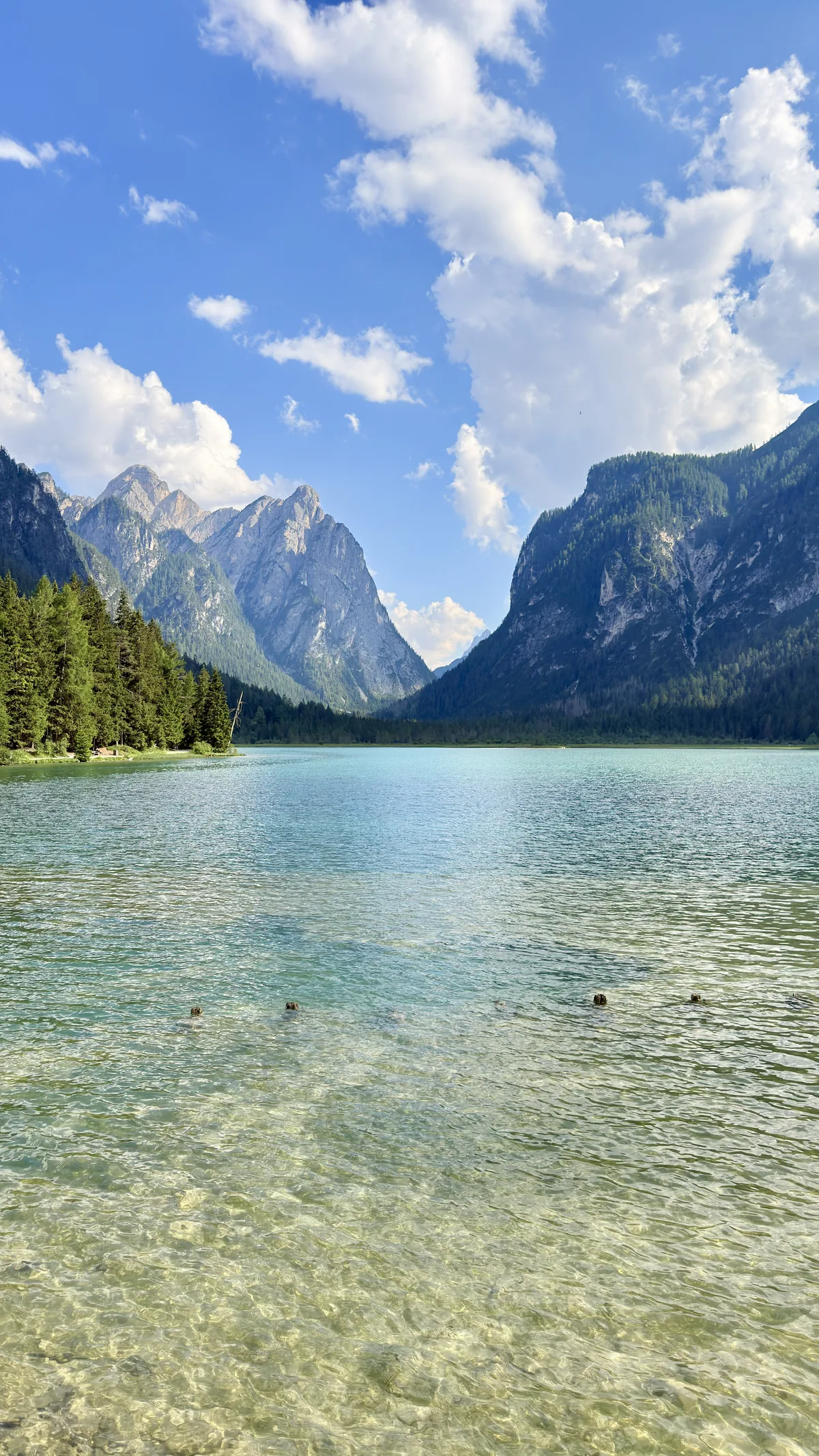 Turquoise water of a lake surrounded by forest and mountains in the Dolomites, with people swimming