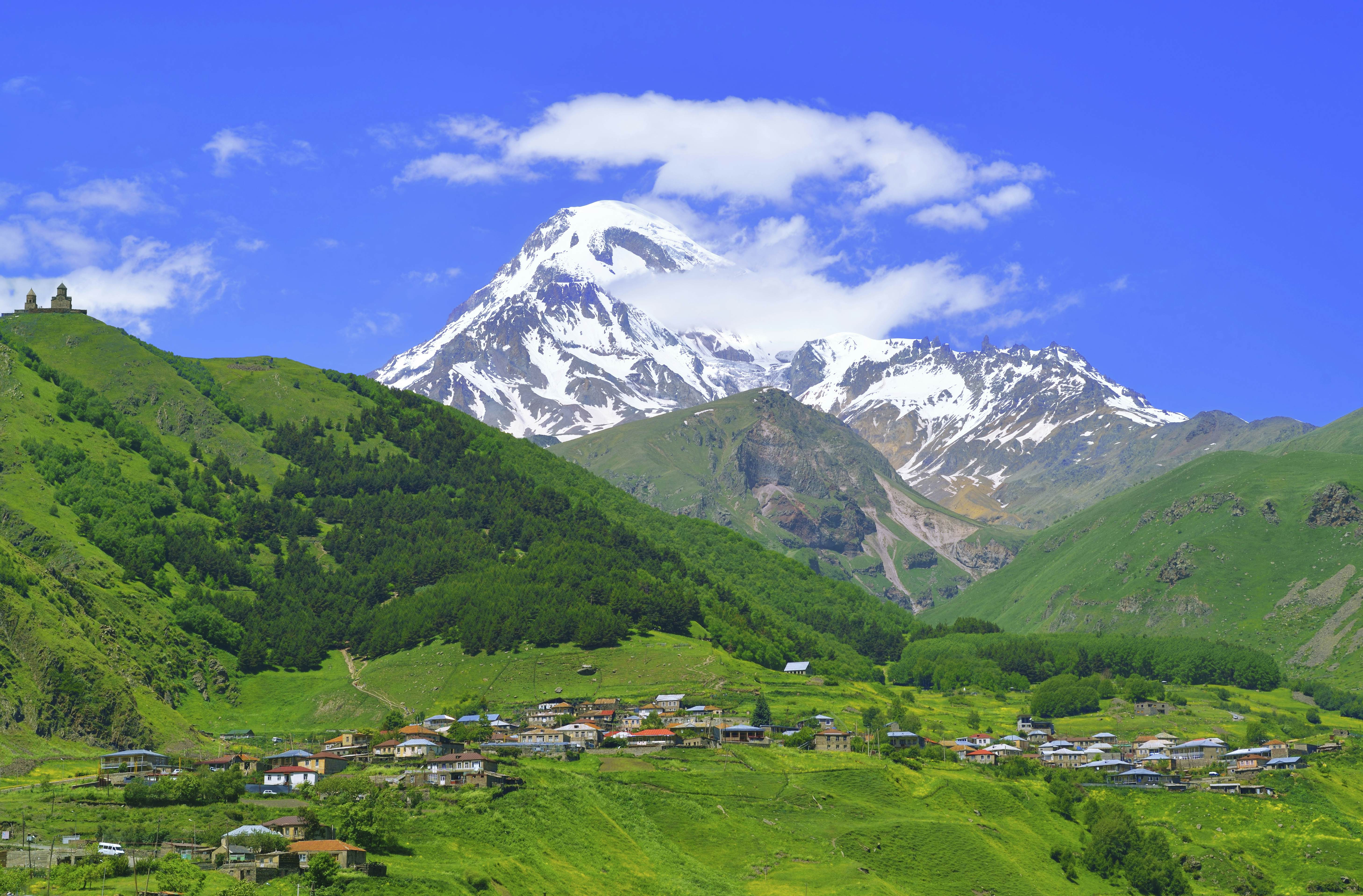 Vila de Stepantsminda cercada pelas montanhas do Cáucaso com a Gergeti Trinity Church ao fundo, Kazbegi, Geórgia