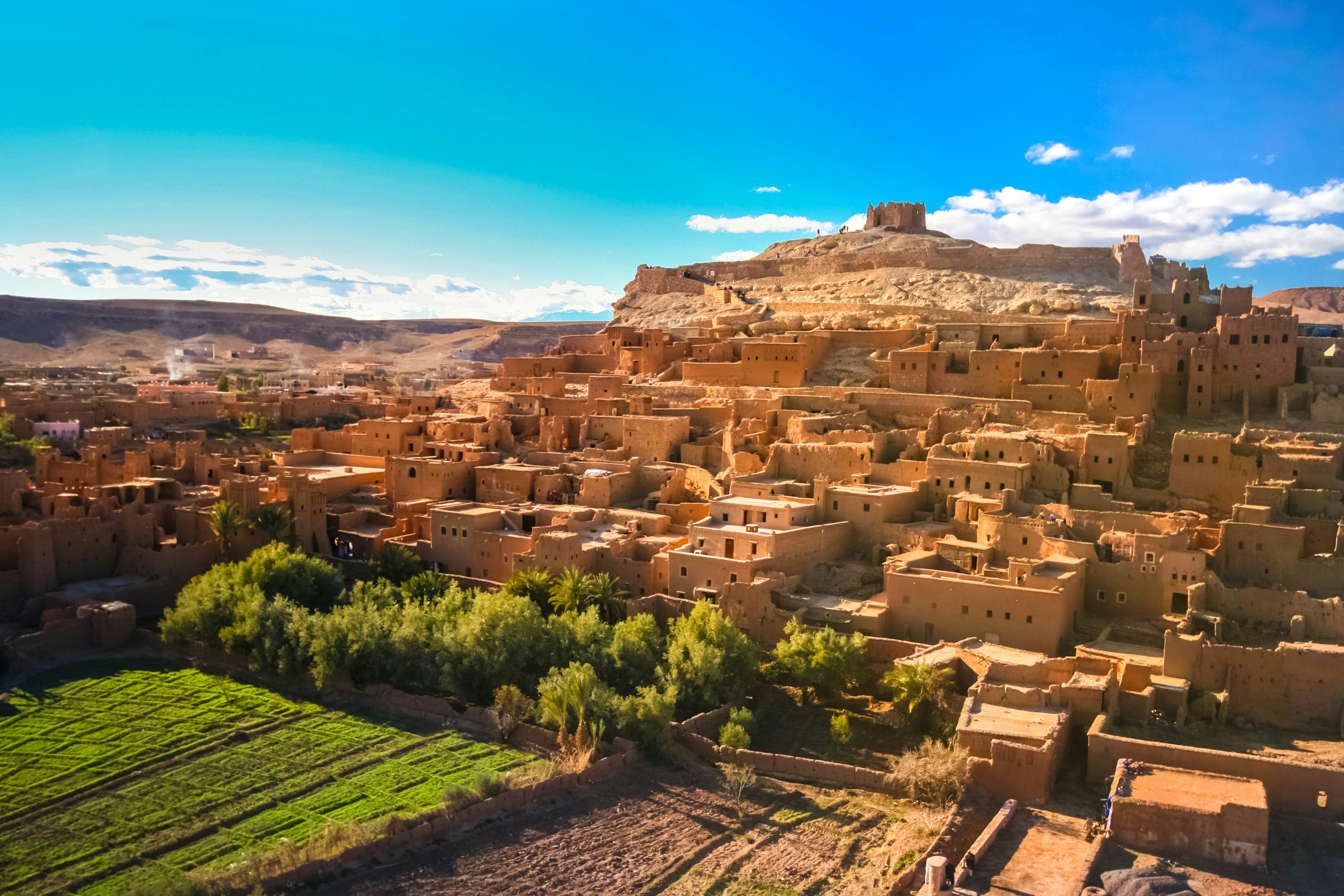 Vista panorâmica de Ait Ben Haddou do alto da kasbah com montanhas e rio ao fundo, sul do Marrocos