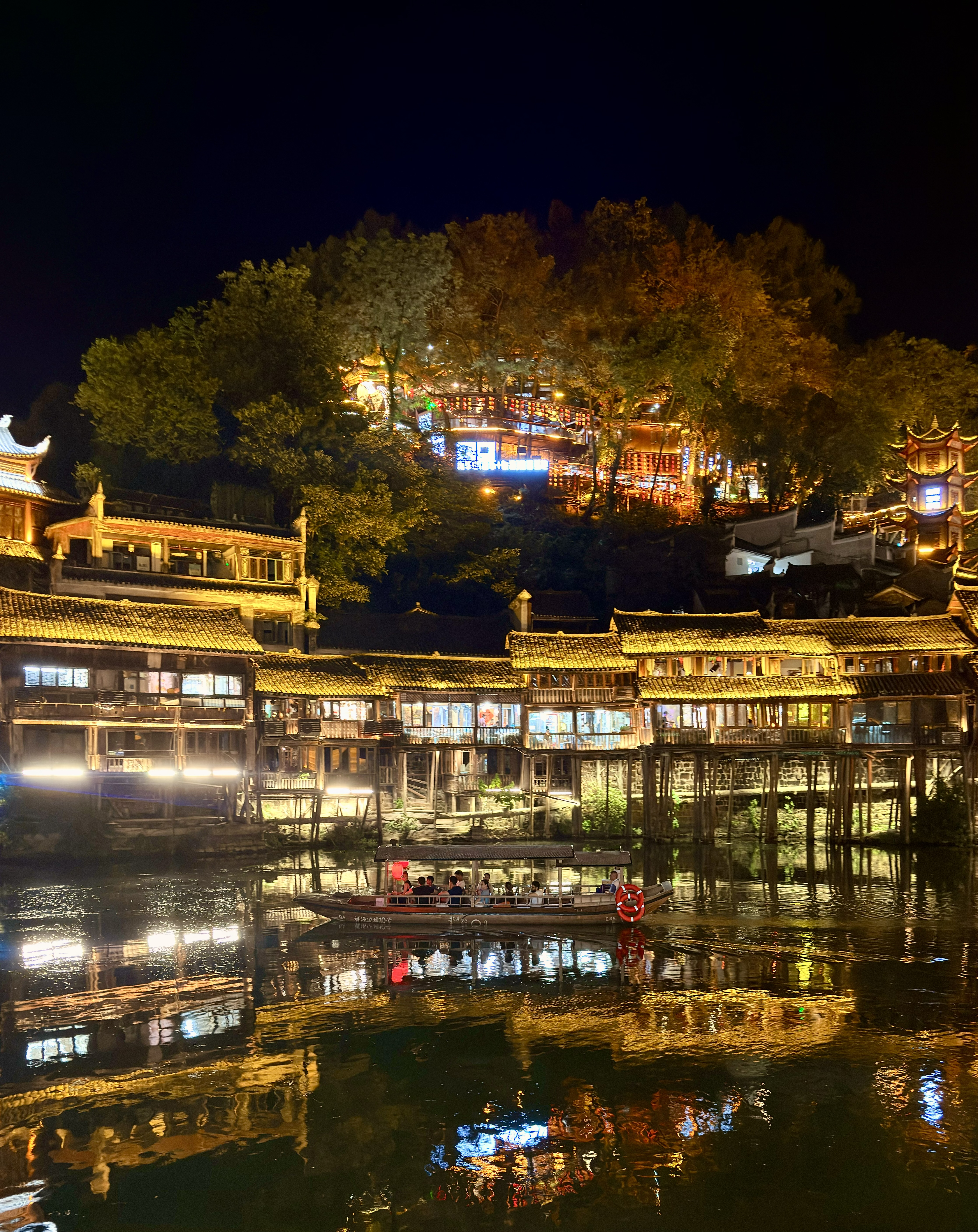 Fenghuang Ancient Town stilt houses illuminated at night with a boat on the Tuojiang river